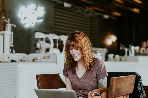 Female, smiling, in front of computer, at restaurant | You will feel happy when you learn these 10 strategies to protect yourself from online trolling and harassment, for artists, writers, and creatives