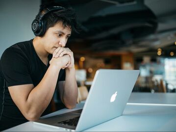 male looking at laptop wearing headphones | creativity coaching online with Cindy Cisneros, Certified Creativity Coach, Career and Life Advice for Creatives